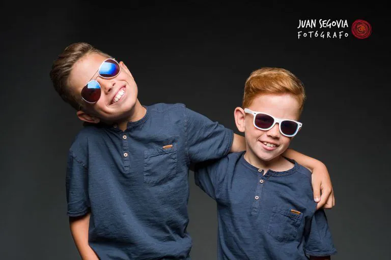 Fotografía de Comunión en Familia - Fotógrafo de Tarragona Fotografía para reportaje de comunión en estudio de dos hermanos sonrientes con gafas de sol en el estudio del fotógrafo Juan Segovia en Tarragona