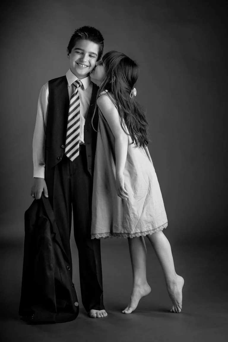 Fotografía de Comunión en Familia - Fotógrafo de Tarragona Fotografia de una nina dando un beso a su hermano para su reportaje de comunion en estudio, por el fotografo Juan Segovia en Tarragona