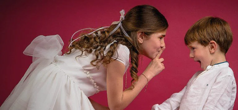 Fotografía de Comunión en Familia - Fotógrafo de Tarragona Fotografia de una nina haciendo callara a su hermano para su reportaje de comunion en estudio, por el fotografo Juan Segovia en Tarragona