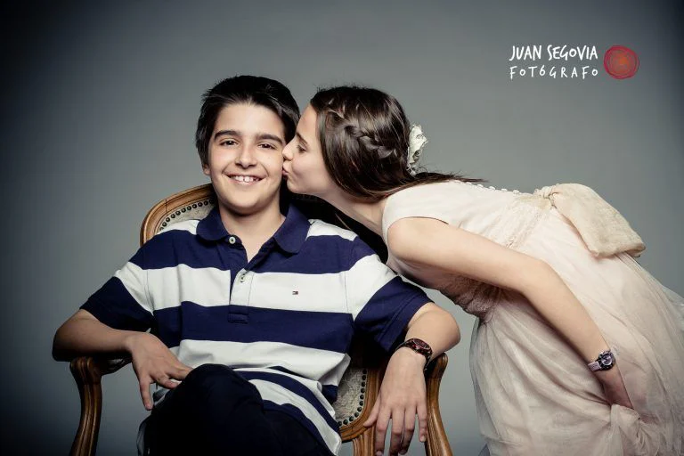 Fotografía de Comunión en Familia - Fotógrafo de Tarragona Fotografía en estudio de una niña besando a su hermano, para su reportaje de fotografía de comunión en familia, por el fotógrafo Juan Segovia de Tarragona