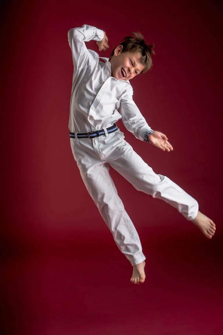 Galería de Fotos de Niños de Comunión en Estudio - Fotógrafo de Tarragona Fotografia de un nino con gafas saltando de lado y riendo para su reportaje de comunion en el estudio de Juan Segovia en Tarragona