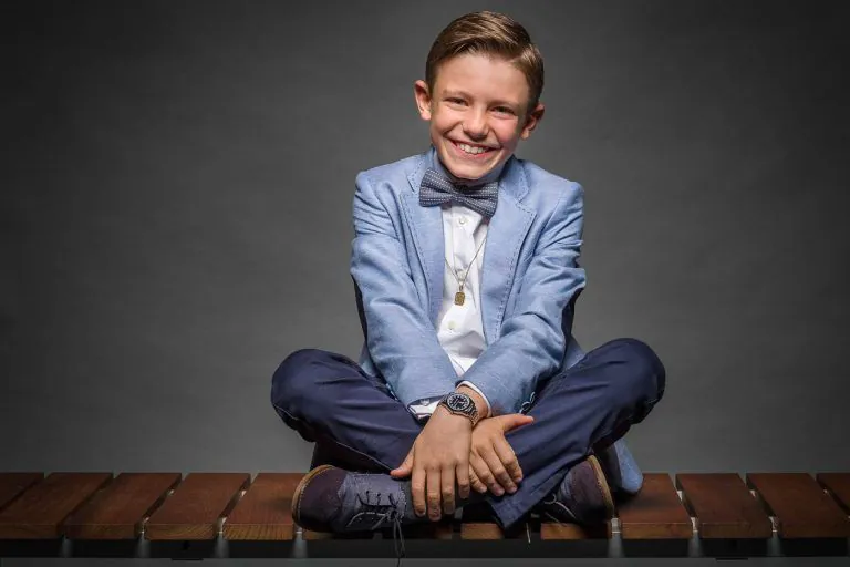 Galería de Fotos de Niños de Comunión en Estudio - Fotógrafo de Tarragona Fotografia de un nino con pajarita riendo sentado piernas cruzadas sobre un banco para su reportaje de comunion en el estudio de Juan Segovia en Tarragona