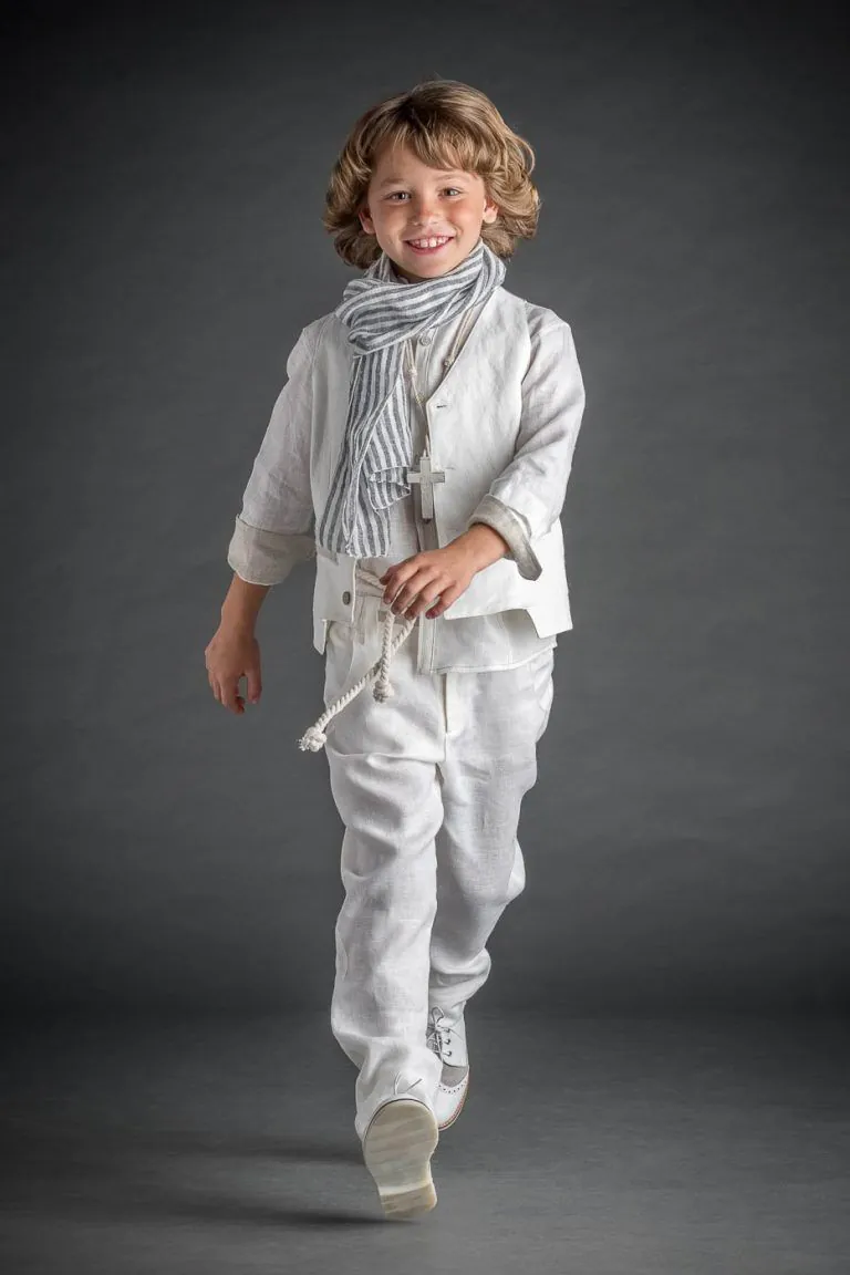 Galería de Fotos de Niños de Comunión en Estudio - Fotógrafo de Tarragona Fotografia de un nino con traje blanco y fulard satando y sonriendo para su reportaje de comunion en el estudio de Juan Segovia en Tarragona