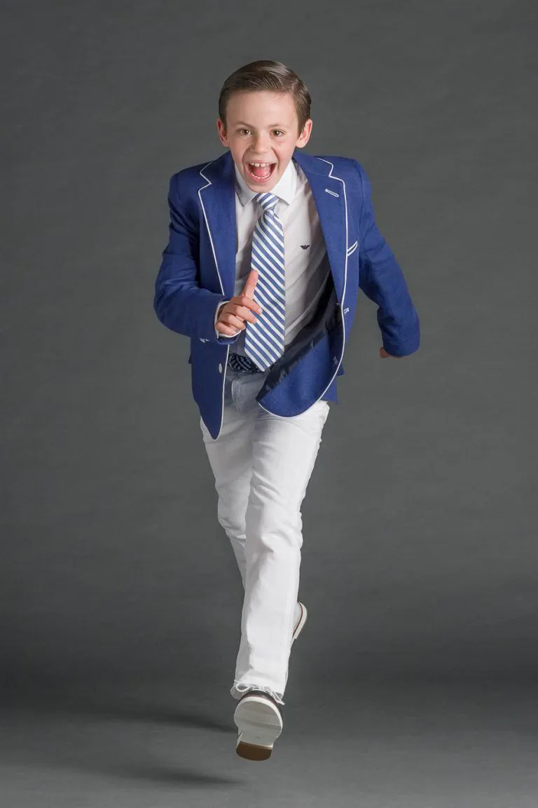 Galería de Fotos de Niños de Comunión en Estudio - Fotógrafo de Tarragona Fotografia de un nino repeinado con americana azul saltando para su reportaje de comunion en el estudio de Juan Segovia en Tarragona