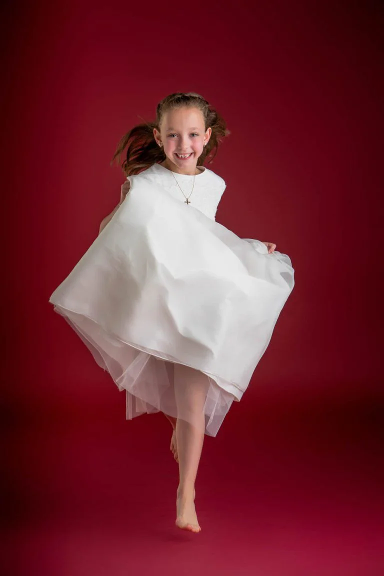 Galería de Fotos de Niñas de Comunión en Estudio - Fotógrafo de Tarragona Fotografia de una nina corriendo sobre fondo rojo para su reportaje de comunion en el estudio del fotografo Juan Segovia en Tarragona